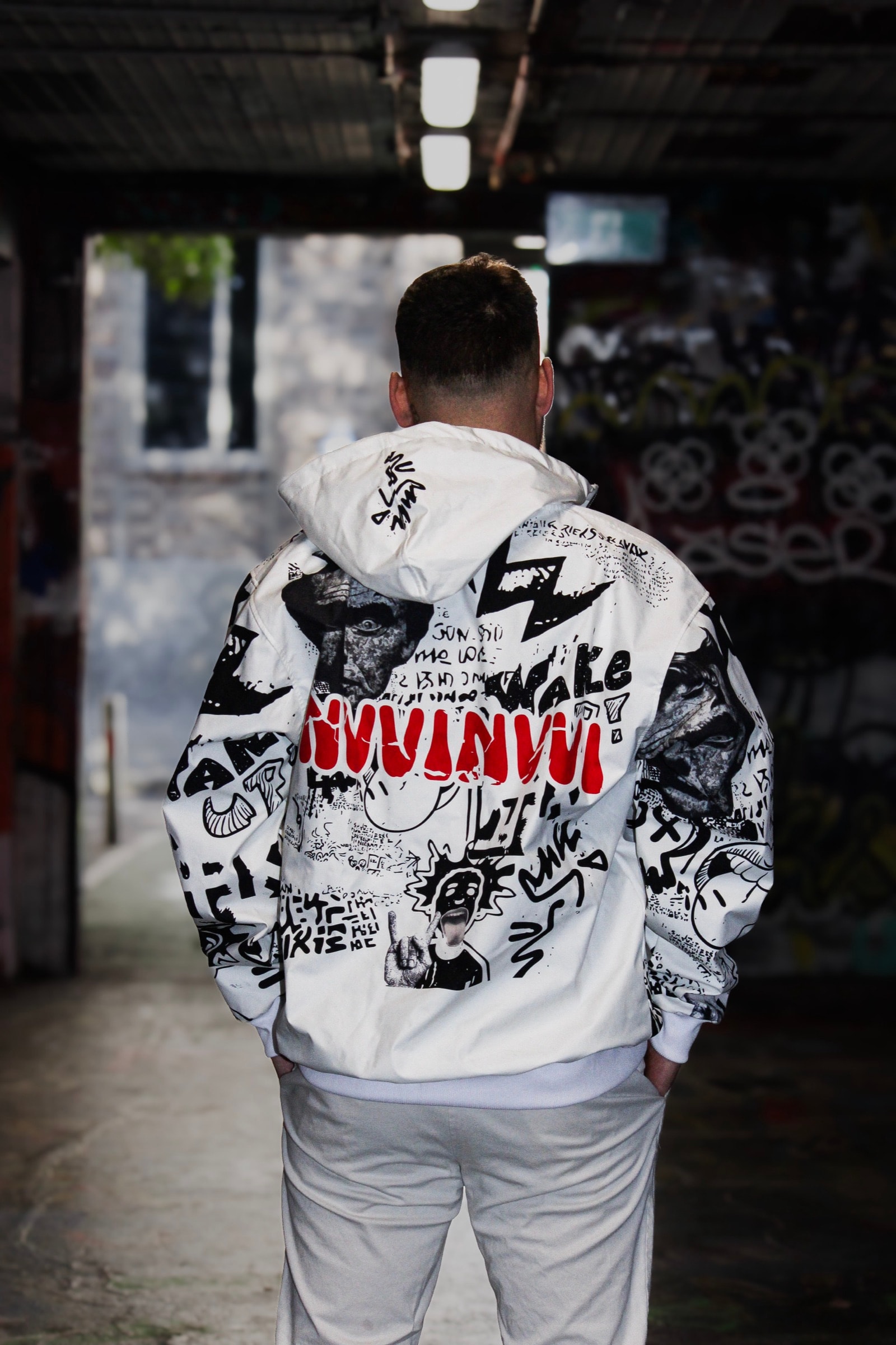 Veste graffiti blanche VINV portée de dos, print NVVINVVI rouge, dans un tunnel couvert de graffitis