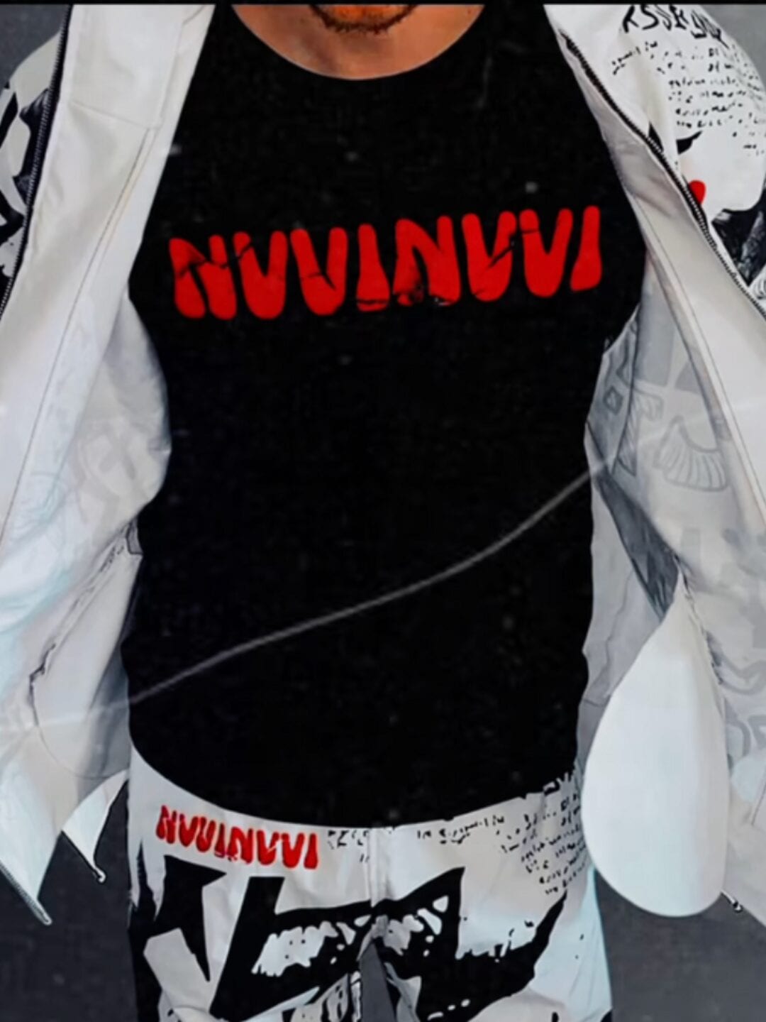 Ensemble porté de face : veste graffiti blanche ouverte sur un t-shirt noir à logo NVVINVVI rouge et un pantalon graffiti blanc.
